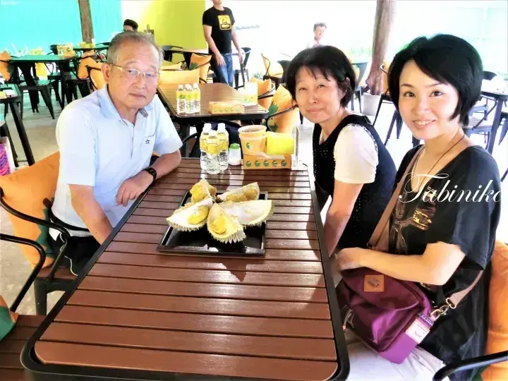 Three people enjoy durian at an outdoor cafe in Malaysia.