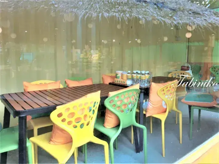 Colorful outdoor seating area with yellow and green chairs, orange cushions, and a thatched roof at a DurianBB cafe.