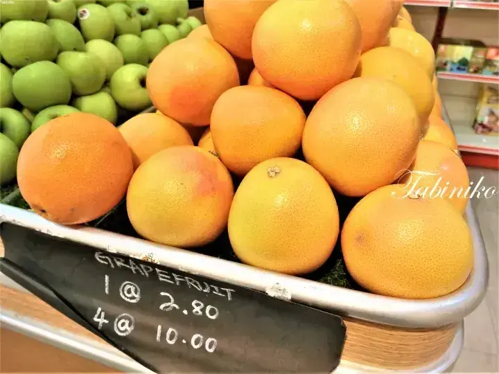 Fresh grapefruits and green apples displayed in a market bin with a chalkboard price sign.