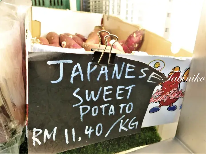 箱にクリップされた「Japanese Sweet Potato RM 11.40/KG」と書かれたチョークボードの看板。