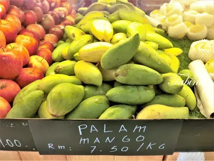 Fresh Palam mangoes displayed at a market stall alongside red apples, priced at RM 7.50 per kg.