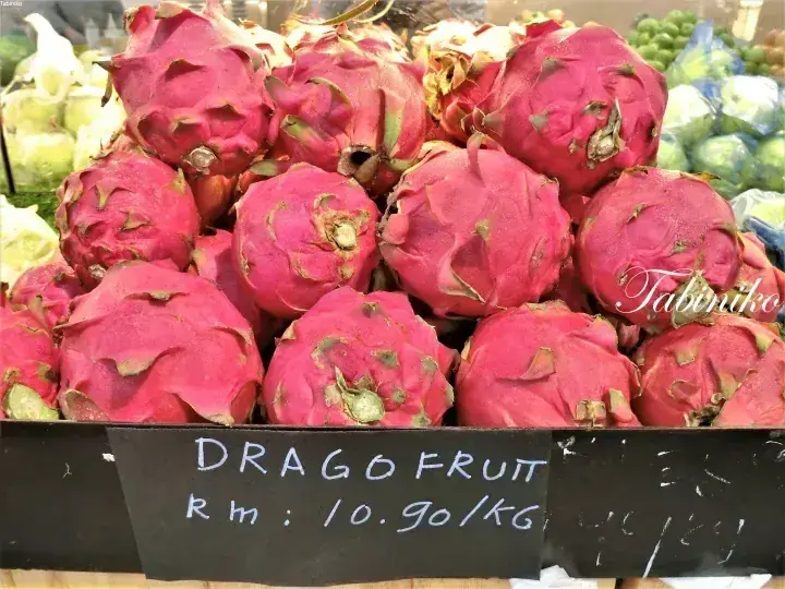 Fresh dragon fruits displayed in a market with a sign showing the price at RM 10.90 per kg.