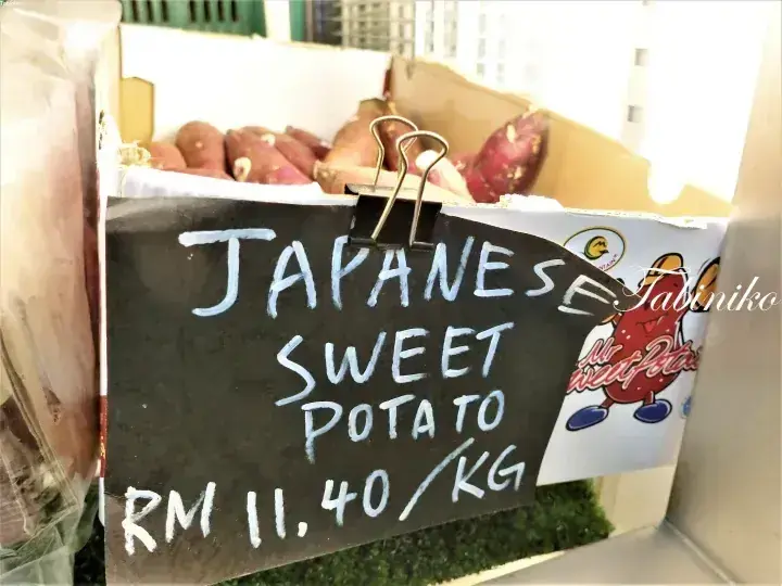 A chalkboard sign reading Japanese Sweet Potato RM 11.40/KG clipped to a box of sweet potatoes.