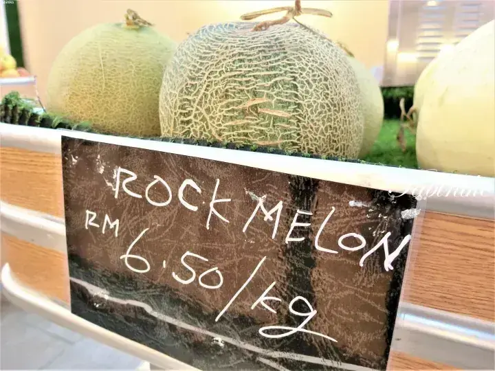 Rock Melon priced at RM 6.50 per kg displayed in a wooden crate at a market.