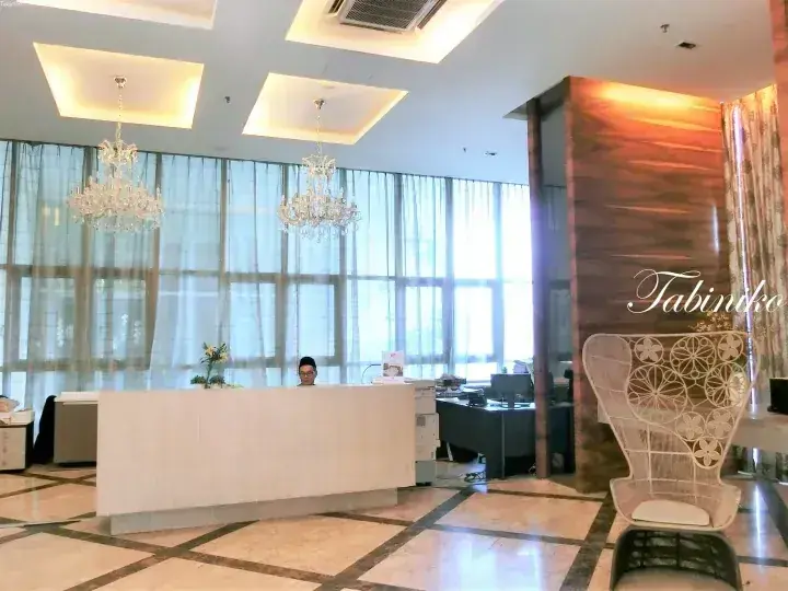Bright hotel lobby with a reception desk, crystal chandeliers, and a decorative white chair.
