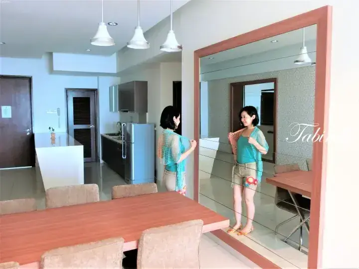 Woman in blue cardigan and shorts admires her reflection in a large mirror in a modern apartment dining area.