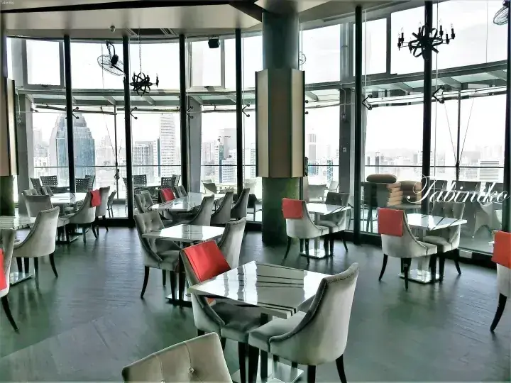 Modern dining area with grey chairs and orange cushions overlooking the Kuala Lumpur city skyline through floor-to-ceiling windows.
