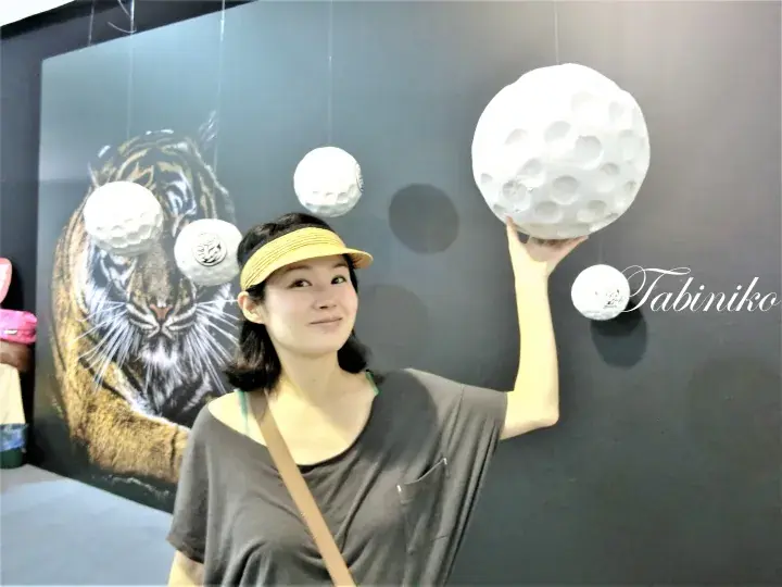 Woman posing with giant golf balls near a tiger mural at a golf-themed attraction.