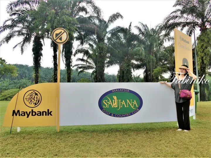 Woman posing beside a Maybank Saujana Golf & Country Club sign with palm trees in the background.