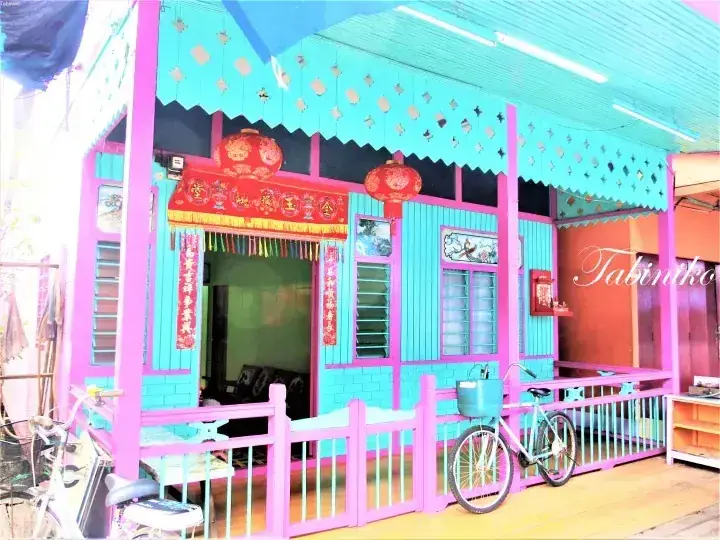 A vibrant turquoise and pink traditional house with red lanterns and Chinese couplets, featuring a bicycle parked on the porch.