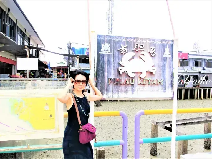 Woman posing in front of the Pulau Ketam sign featuring a crab and Chinese characters.