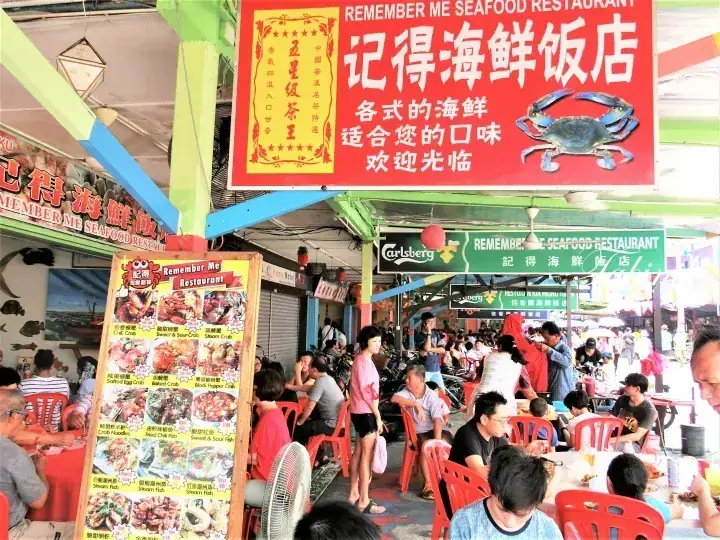 Bustling outdoor dining area at Remember Me Seafood Restaurant with patrons eating at red tables under a large red sign.