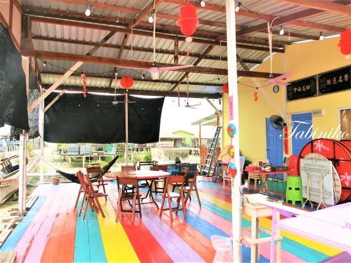 レインボーの床と赤い提灯が特徴的な、水辺のレストランのカラフルな木製デッキ。