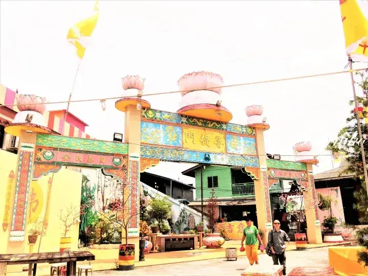 Colorful entrance gate with lotus decorations at a Malaysian temple, featuring traditional Chinese architecture and visitors walking through.