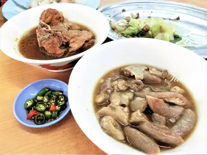 A bowl of braised pork intestines and a bowl of pork rib soup served with chili sauce and vegetables.