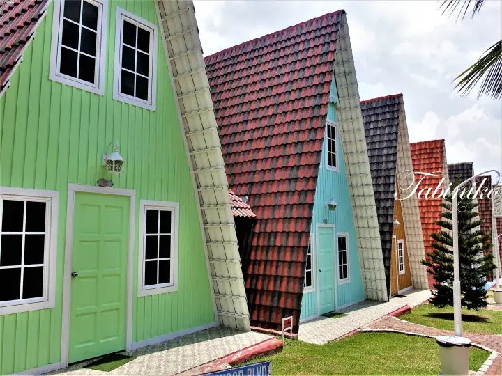 Colorful A-frame cabins with tiled roofs at Tabinka Resort, featuring green, blue, and yellow units with white trim.