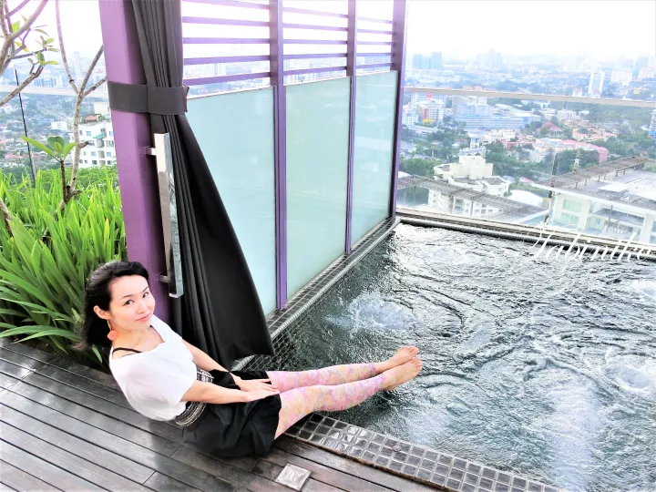 Woman relaxing by a rooftop infinity pool with a city view at a luxury Kuala Lumpur hotel.