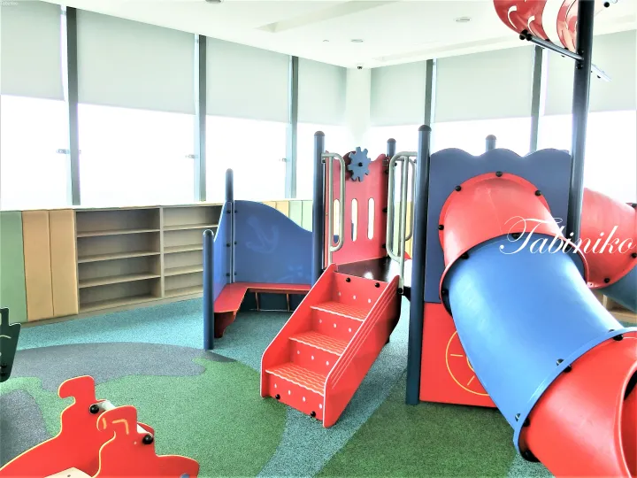 Colorful indoor playground with red stairs and blue slide in a bright room with large windows