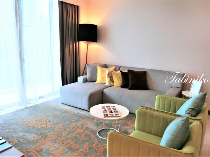 Modern living room with grey sectional sofa, green armchairs, and patterned carpet in a property interior.