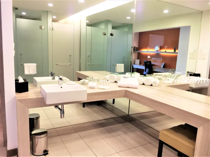Modern hotel bathroom with dual sinks, large mirror, and neatly arranged towels on a light wood vanity.