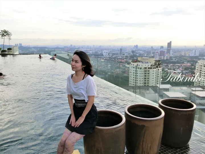 Woman sitting by an infinity pool overlooking the Kuala Lumpur city skyline at dusk.