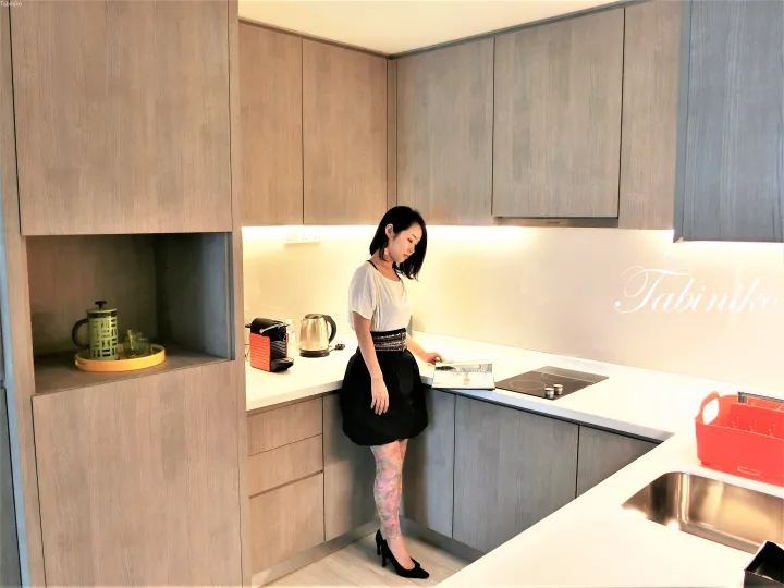 Woman standing in a modern kitchen with light wood cabinets and a Nespresso machine.
