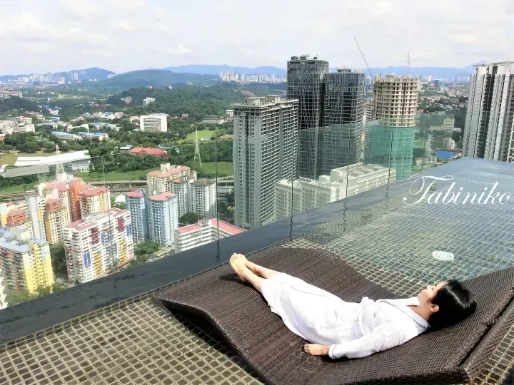 在屋頂無邊際泳池躺椅上放鬆的女性,俯瞰吉隆坡城市天際線和周圍山丘。