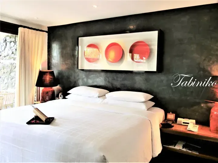 Modern hotel bedroom with dark accent wall, white linens, and red circular art above the bed.