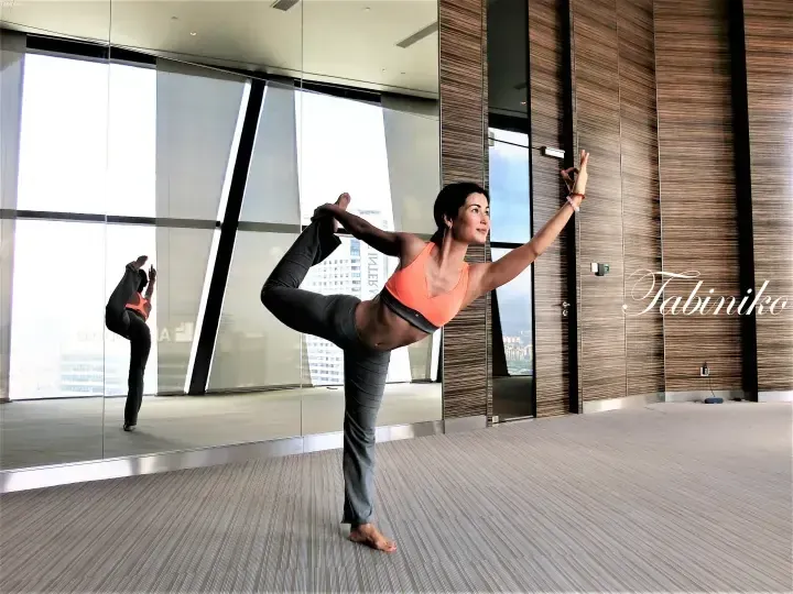 Woman practicing yoga in a high-rise hotel room with floor-to-ceiling windows overlooking the city skyline.