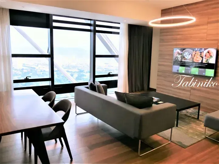 Modern living room with grey sofa, dining table, and large windows overlooking the city skyline.