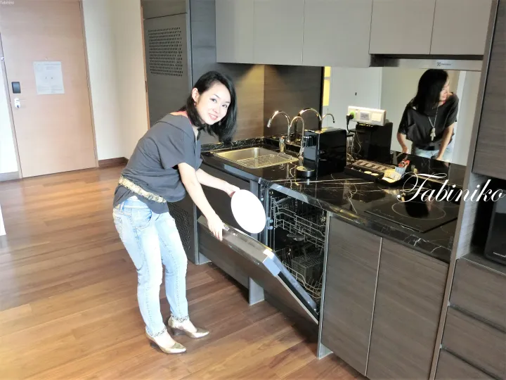 黒い大理石のカウンターとステンレス製家電が特徴のモダンなキッチンで食洗機を開ける女性