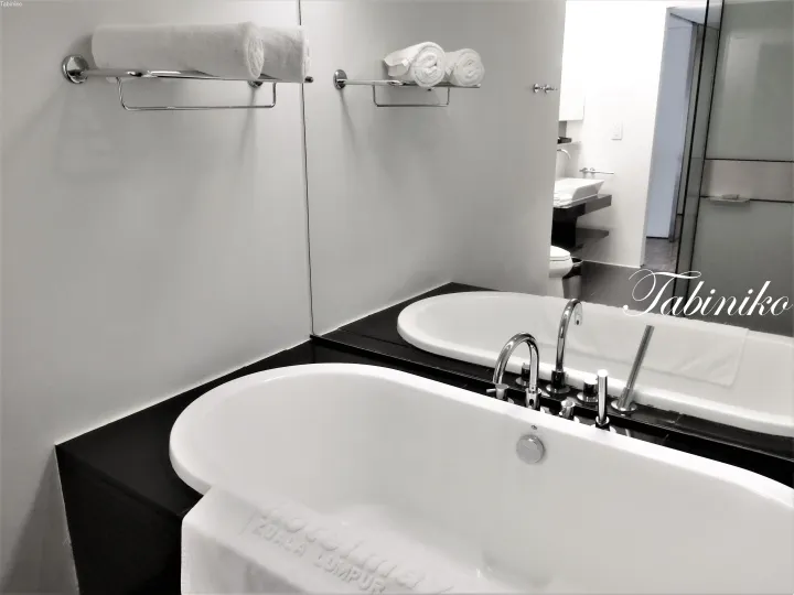 白いバスタブ、クローム製設備、整然と並んだタオルが映えるモダンなホテルバスルーム。