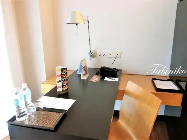 Hotel Maya Kuala Lumpur desk with water bottles, lamp, and brochure.