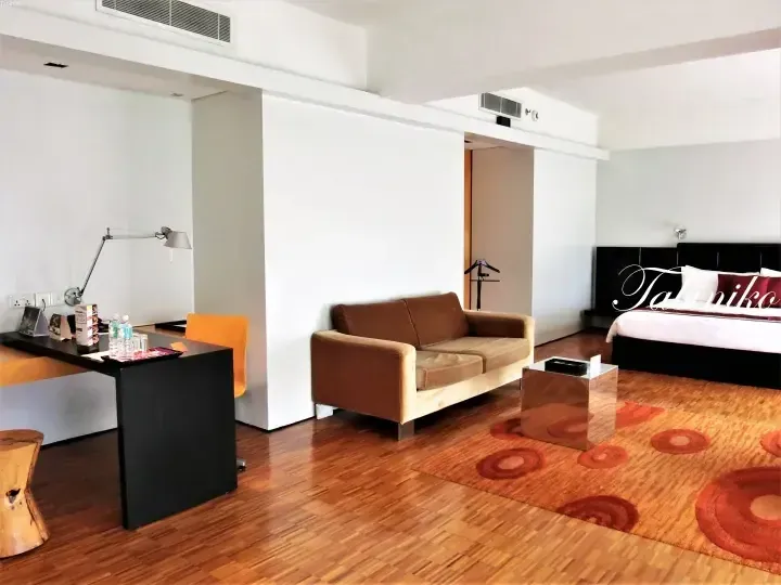 Modern hotel suite interior featuring a brown sofa, wooden desk, and bed with orange patterned rug.