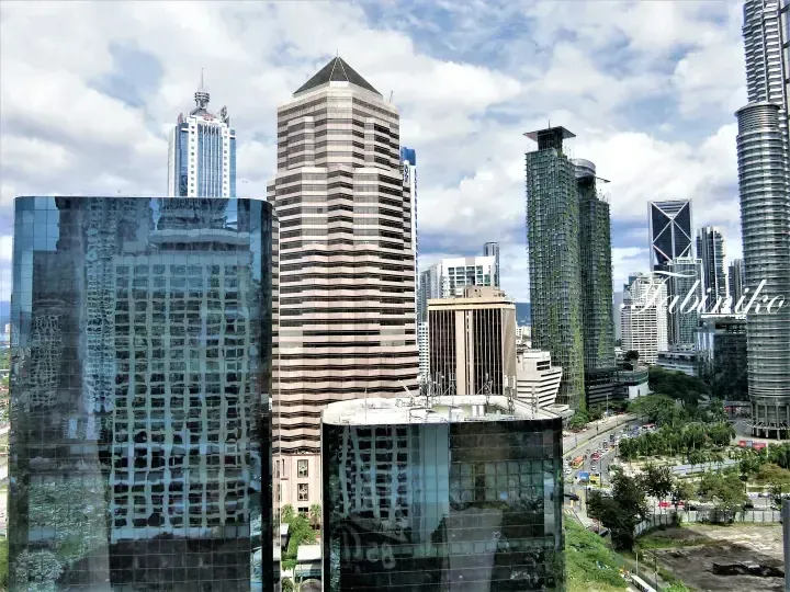 Kuala Lumpur cityscape featuring Menara Maybank and modern skyscrapers under a cloudy sky.