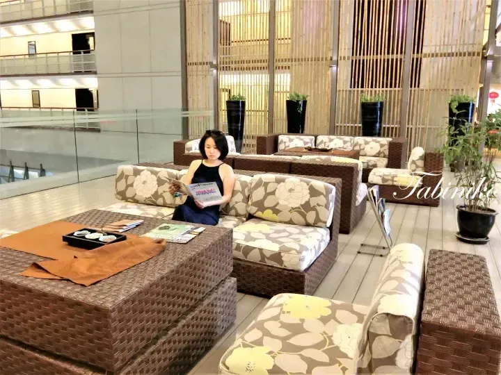 Woman reading a magazine in a modern lounge with rattan furniture and bamboo screens at a Malaysia property.