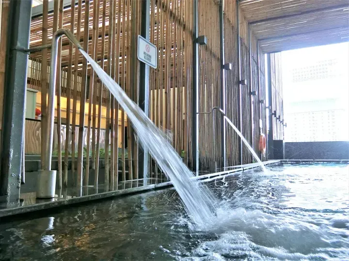 Water jets flow into a pool at a modern resort with bamboo walls and a no diving sign.