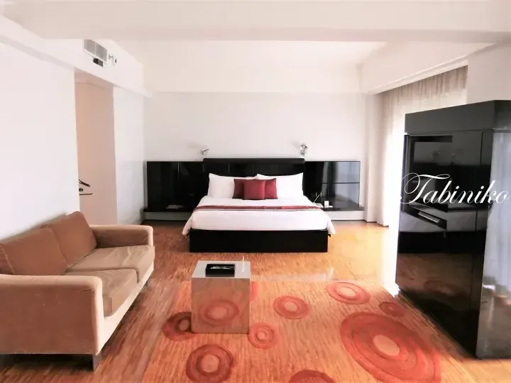 Modern hotel suite with a king bed, brown sofa, and circular rug pattern.