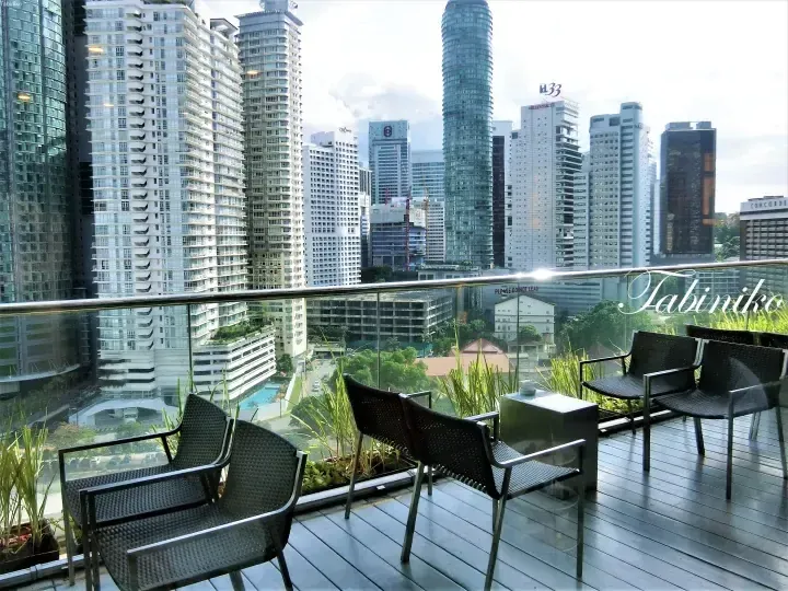 Balcony terrace with wicker chairs overlooking Kuala Lumpur skyline featuring KL33 and Prudential Tower