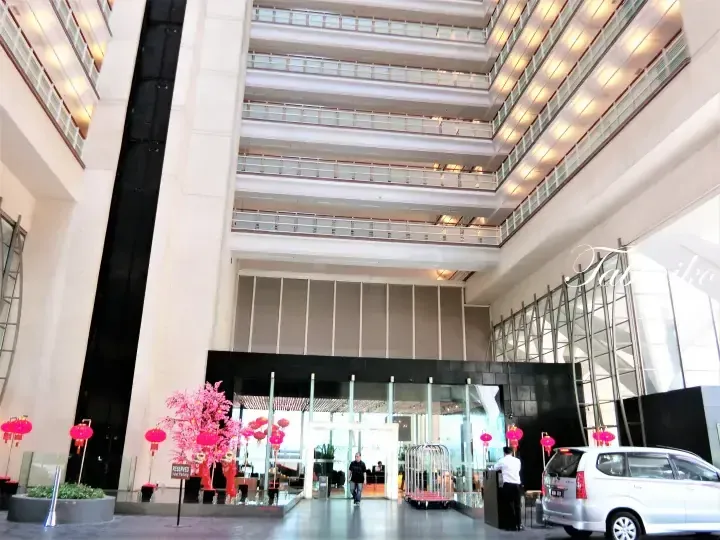 Grand atrium entrance of a hotel with multiple floors, red lanterns, and a valet parking area.