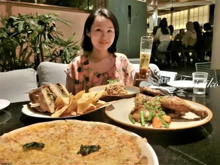 Woman dining at a restaurant with pizza, roast chicken, and sandwich.