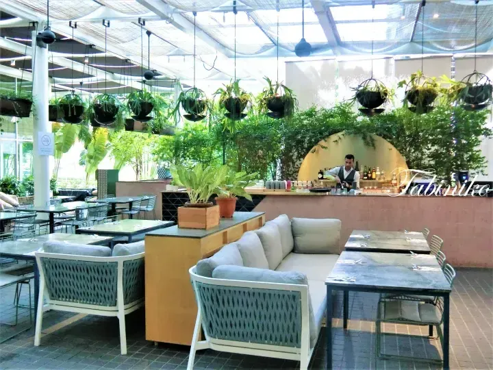 Modern restaurant interior with hanging plants, comfortable seating, and a bar area in a bright, open space.
