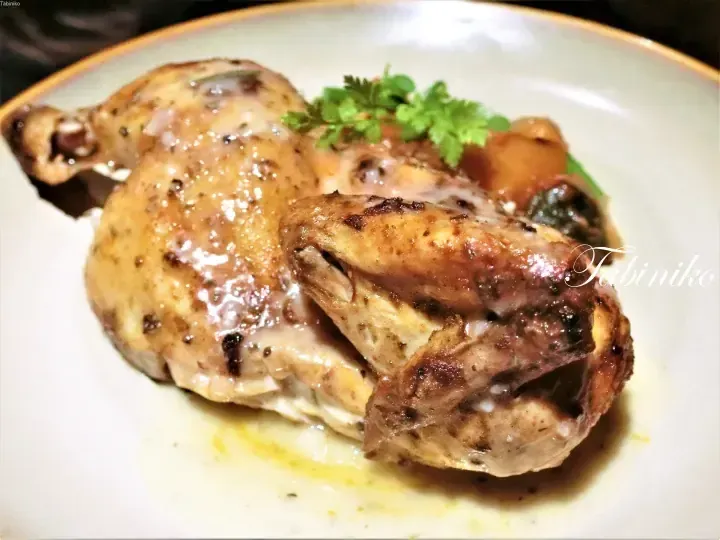 Golden roasted chicken pieces with herbs and sauce on a white plate