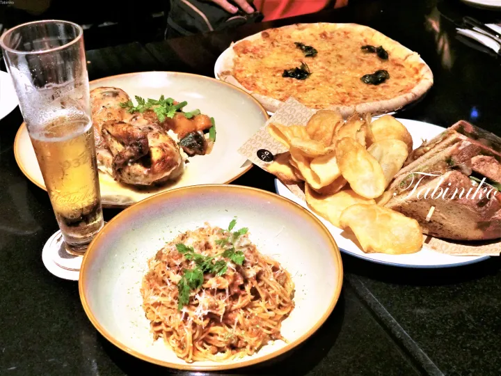 ピザ、パスタ、チキン、サンドイッチ、ポテトチップス、ビールが並ぶ食卓