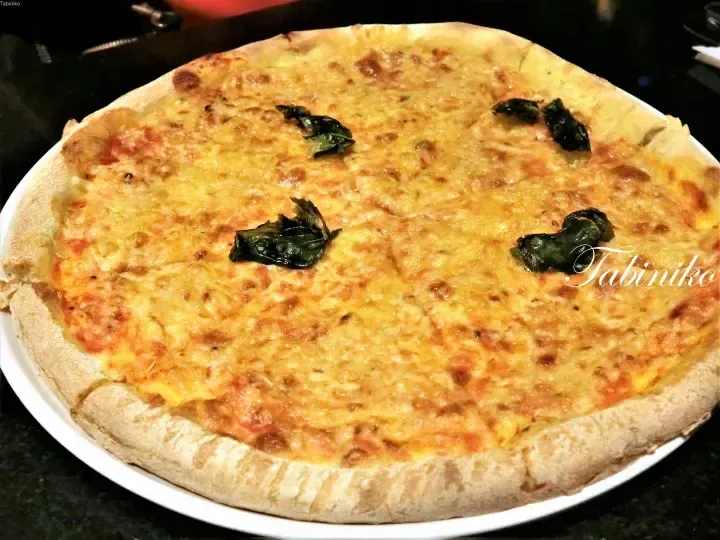 Freshly baked pizza with melted cheese and basil leaves on a white plate