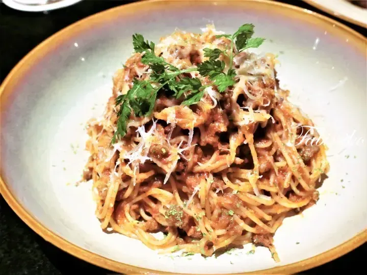 Spaghetti bolognese topped with grated cheese and fresh parsley on a ceramic plate