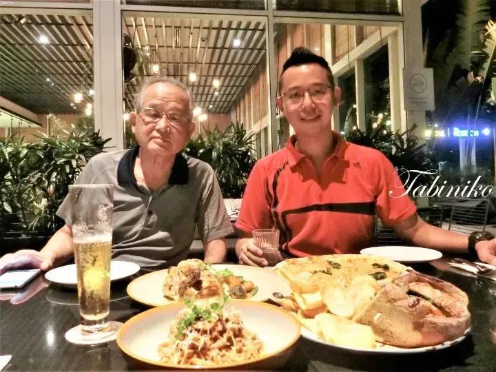 Two men dining at an outdoor restaurant table with plates of food and a glass of beer.