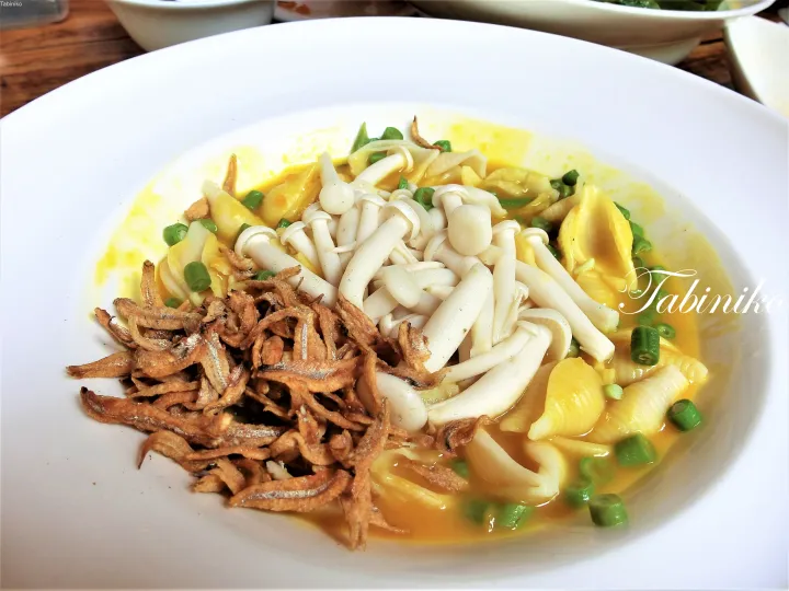 エノキ茸、イワシの煮付け、刻みネギをトッピングした黄色い麺料理。