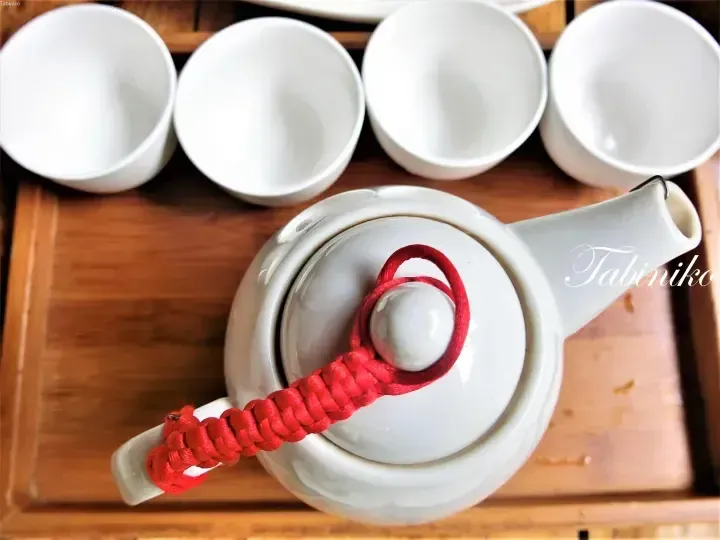 White ceramic teapot with red cord and four matching cups on wooden tray
