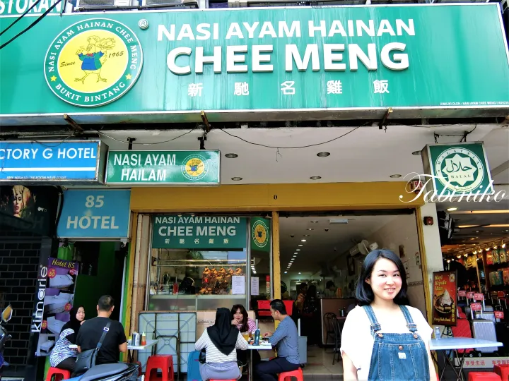 ブキットビンタンのNasi Ayam Hainan Chee Mengレストラン前でポーズをとる女性と、屋外で食事をする客たち。